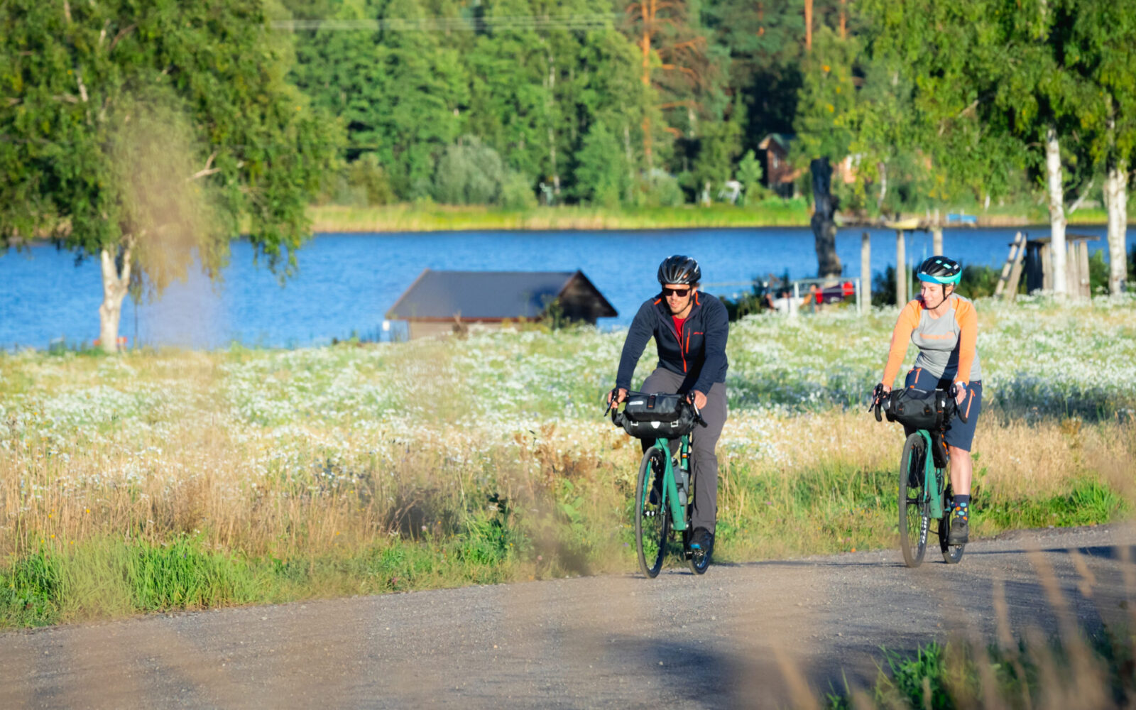 Mies ja nainen pyöräilemässä maalla järven siintäessä horisontissa kesällä.