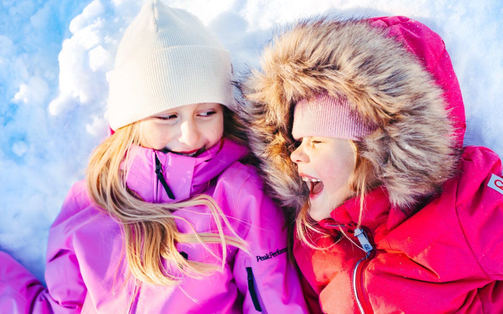 Kaksi lasta nauraa lumessa